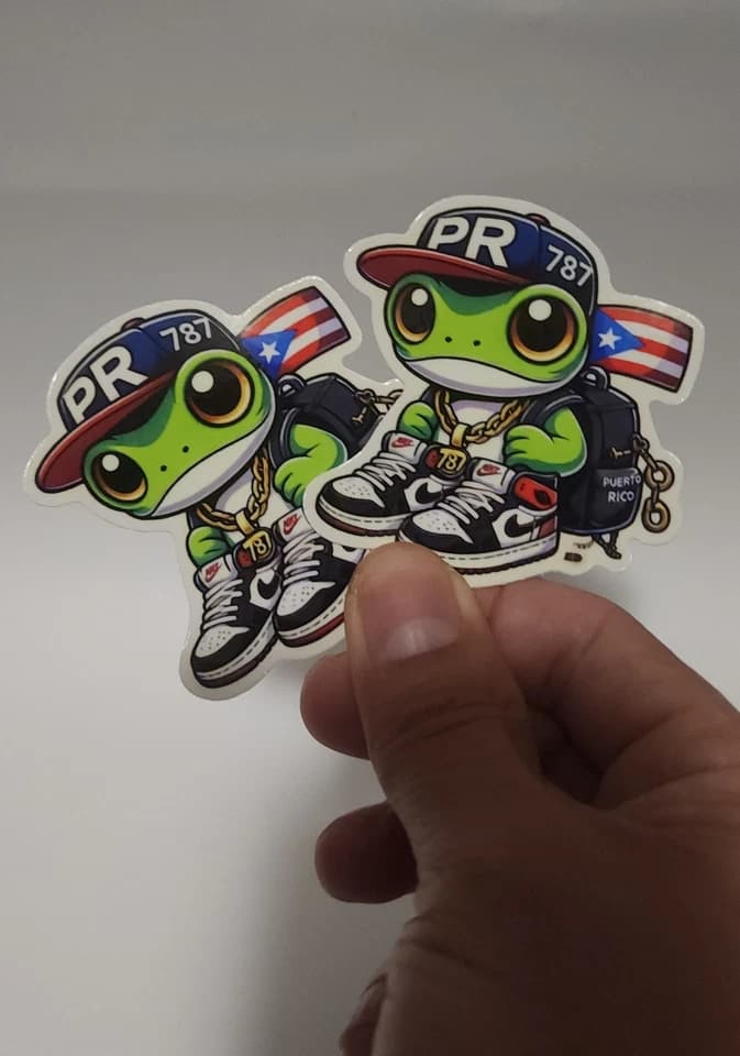Dos stickers del coquí 787 sostenidos en mano